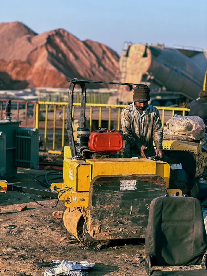 A construction worker operates machinery outdoors amidst equipment at a site.